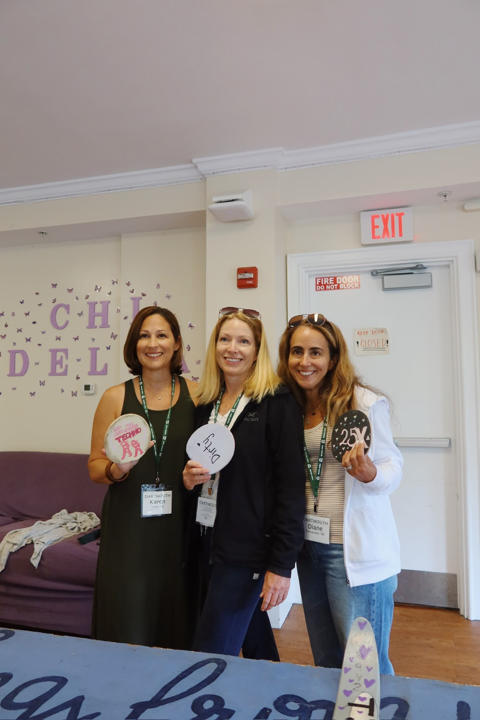 Three alumnae in reunion name tags holding their painted paddles in the haus