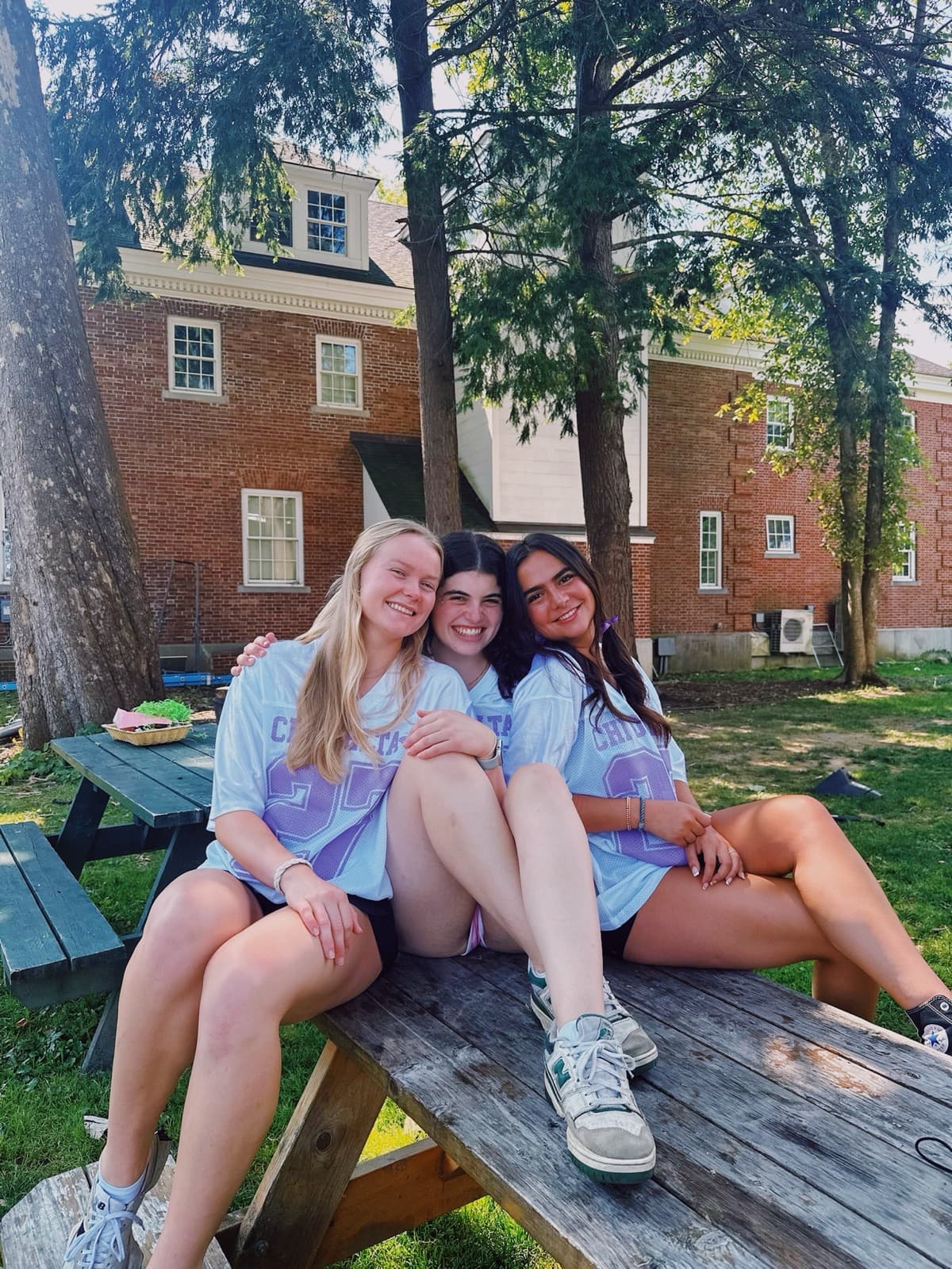 Three sisters in Chi Delta jerseys on a picnic table