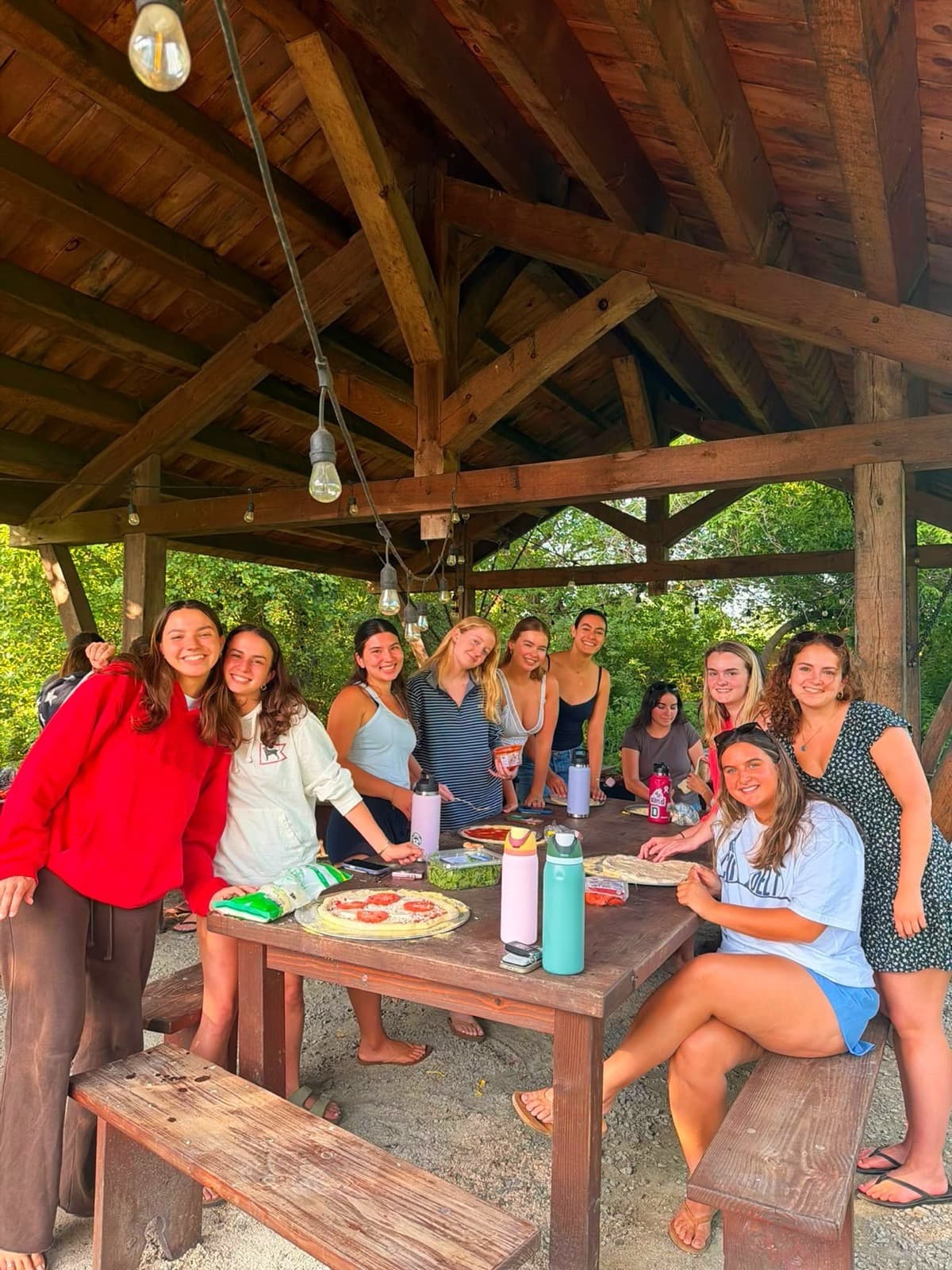 A large group of sisters making pizza under a pavilion