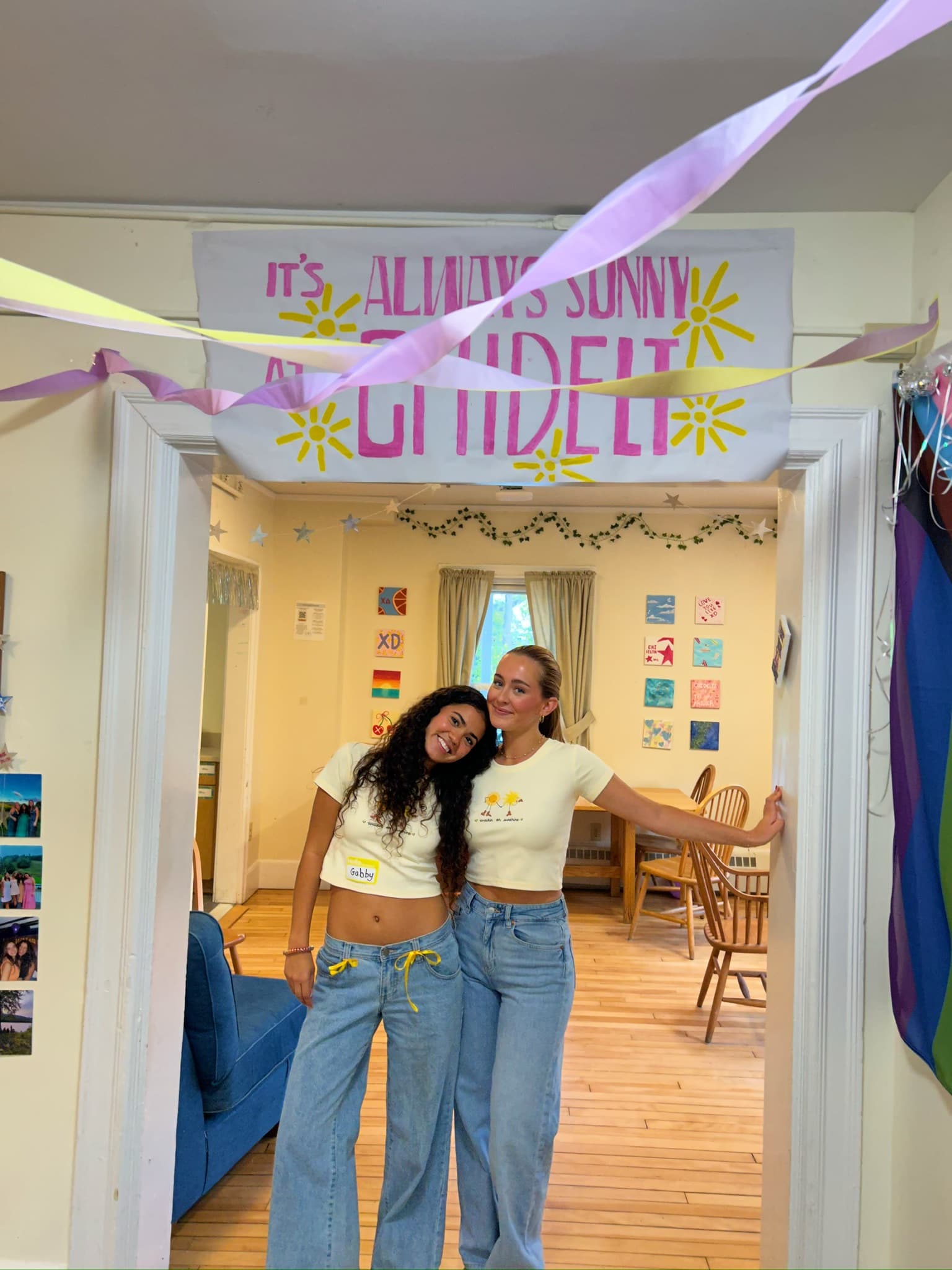 Two sisters in the haus doorway under the "It's Always Sunny at Chidelt" banner
